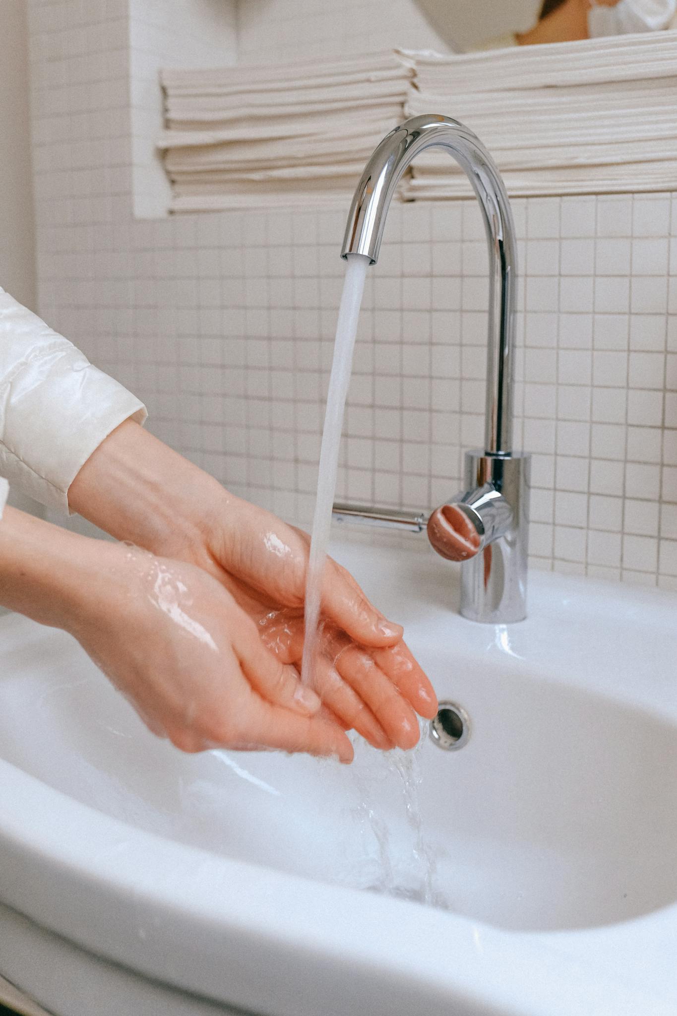 Close-up of hands being washed under running water in a bathroom sink for hygiene and virus prevention.